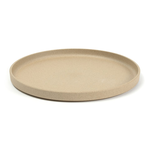 3/4 view of a round, tan plate on a white background. The color and texture is like pressed sand. Plate has straight sides with a lip protruding above the flat surface.