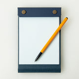 Palm-sized refillable snap pad with graph paper, featured in dark blue. A yellow and black pen rests on top of the pad.