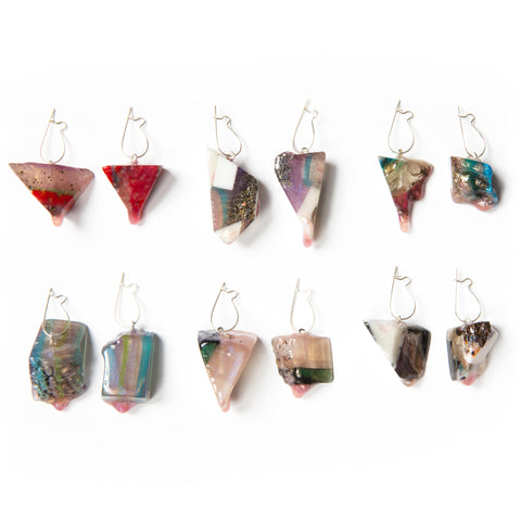 Two rows of three pairs of irregularly shaped, dangly earrings. The earrings are all different colors and shapes, with shimmer, striations, colors, and miscellaneous materials embedded in resin.