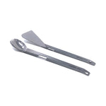 The Splitter shown as two separate titanium pieces, the long spork and spatula laying side by side. Both have serrating around the edges. 