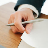 Detail of a hand holding the Handmade Stainless Steel Pen and flipping the corner of a notebook.