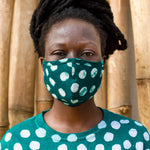Model wearing a face mask made of a deep green fabric printed with white polka dots, and a matching shirt.