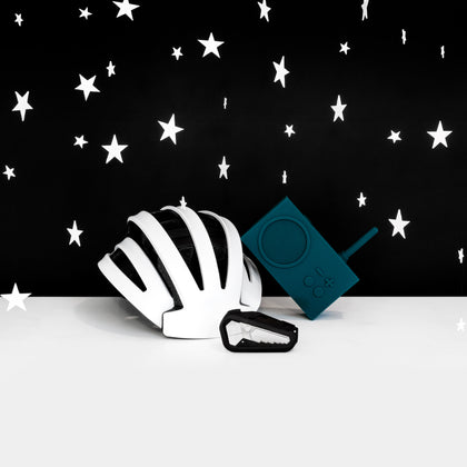 A group of three objects (a white helmet, a black multitool, a minimal teal radio) on a white surface against a black background with white stars hovering around. 