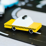 Small, geometric wooden taxi on a black and white road surface.