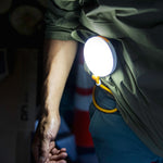 Illuminated, disk-shaped light supported by its flexible, yellow arm which is wrapped around a person's belt loops.