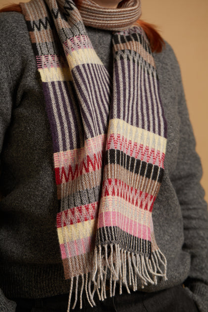 Striped scarf with fringes worn by a person in a gray sweater against a beige background
