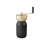 Sleek hand-crank coffee grinder with a black jar-shaped storage base and brushed brass grinding bowl and handle with a black grip.