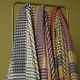 Three patterned scarves hanging on a green rack against a green background