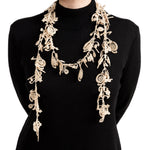 View of a person in a black sweater  modeling the beige, open-ended single-strand lace necklace with pieces resembling  hanging watch springs and gears, stylishly draped in a loose coil around the neck with long dangling ends.