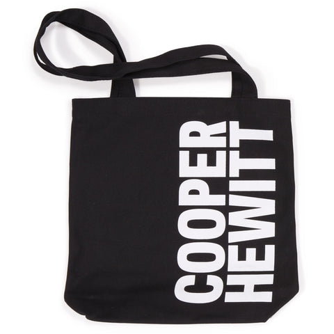 Black tote bag with the Cooper Hewitt logo rotated vertically, printed in white on the right half of the front of the bag.