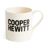 Facing forward, an off-white mug has "Cooper Hewitt" printed in black in all caps. The font is a bold, block, sans-serif style.