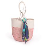 A navy blue scarf with pastel print detail tied around the handle of a red and beige handbag.