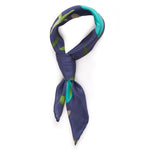 A navy blue silk scarf  with soft shapes in blue and green painted across its center. The scarf is styles in a knot suggesting a way to wear it.