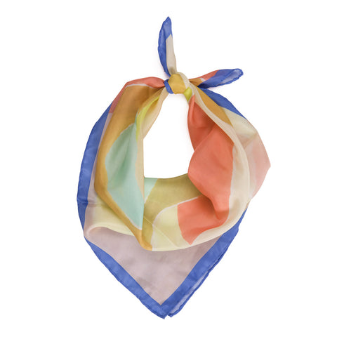 A blush colored scarf with blue trim. A series of shapes are painted in the center in various pastel colors that include a sea foam green, coral, and light yellow. The scarf is tied into a knot at the top in a suggestive style for wearing out.