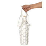 An outstretched hand holds the handles of a small laser cut off-white leather net bag, with a white wine bottle inside, its weight stretching the shape of the bag 