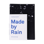 Made by Rain Book; black cover with a few small splashes of white and smaller off-white booklet layered over, with the title in blue [traveling concept #1 booklet]