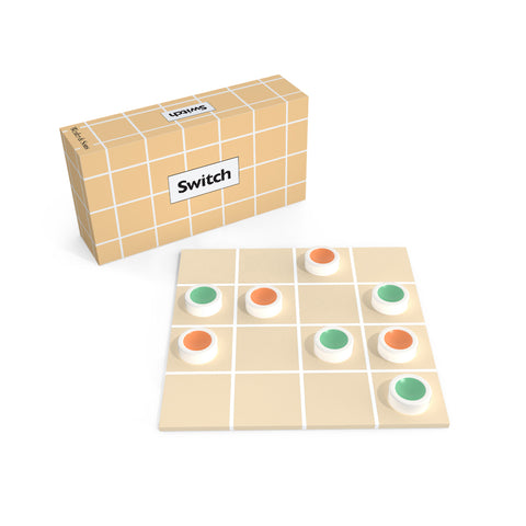 A game in play on a tan square board with a white 4 by 4 grid printed on it. Eight, white, disk-shaped games pieces with colored depressions on the top in either orange or green each sit in their own grid square. The game box with the same pattern as the board and text “Switch” sits in back.