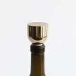 A close up photo of a Mass Wine Stopper inserted into a wine bottle. Its shiny brass finish is reflective.