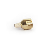 A Mass Wine Stopper lays on its side, its shiny brass finish is reflective.