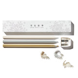 A Snow Pencil set with the box and its contents laid out on a white surface. The shot includes the white snowflake patterned box, three different color metallic pencils, and a white double sharpener. Pencil shavings are strewn about.