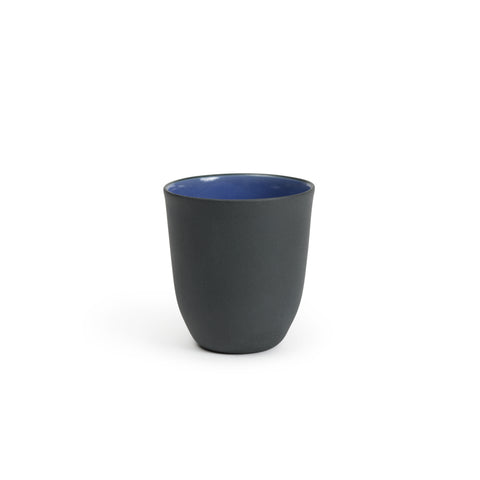 Small porcelain cup with a royal blue glazed interior and unglazed dark gray exterior.