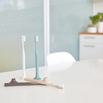 4 toothbrushes on a white countertop. 2 toothbrushes have been placed in their stands, while the other two lay flat on the surface.