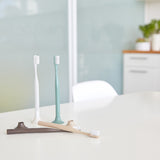 4 toothbrushes on a white countertop. 2 toothbrushes have been placed in their stands, while the other two lay flat on the surface.