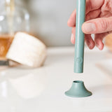 A closeup photo of a light-skinned hand placing a pale green toothbrush into its stand.