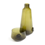 Olive green glass and carafe. Both items are marked with an emblem resembling a coin.