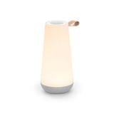 Lit Uma Mini on a white background, showing its tapered, conical body, rounded cup-shaped silver speaker base, flat silver rimmed speaker/dimmer top and handy looped leather side grip.