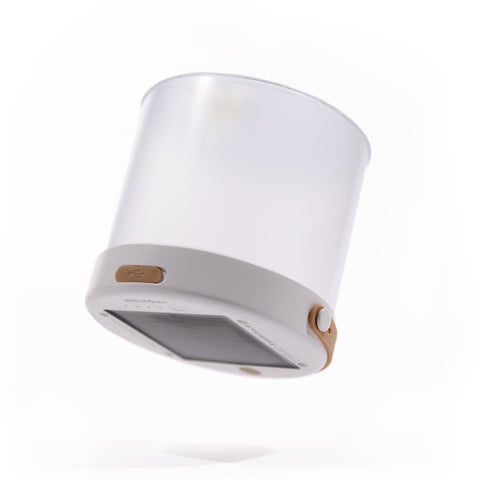 Tilted image of an inflated white cylindrical light with a natural leather carrying strap and solar panel on one end.