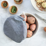 A grey cloth bowl cover is untied and hangs off the edge of a bowl exposing raw potatoes.