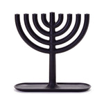 Against a white background is a photograph of a black cast iron menorah; a candelabra with 8 branches in the form of a semi circle each of which connect to a center pole. The center pole forms the 9th branch ‘shammash’ which is slightly higher than the others. The menorah is attached at the bottom to an oval lipped tray.