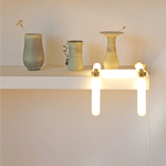 White shelf with vases on top, and a geometrically configured tube light dangling off of one end.