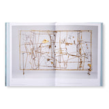 Image of the book spread open to reveal inside pages. Pictured is a hollow three- dimensional wire rectangle sitting on four small feet. Filling the negative space is a tangle of brass rods and geometric shapes that intersect each other at multiple planes. 