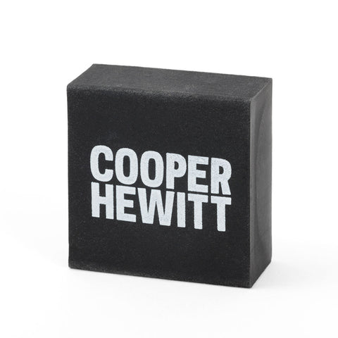 A square black eraser stands on its edge facing forward. "Cooper Hewitt" is printed on the front in white in large block font.