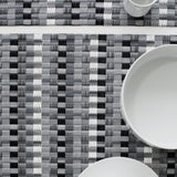 Close up view of one and one-third basketweave placemats with light and dark gray, white and black vertical stripes on a flat woven field of subtle gray and white stripes, with partial views of a white ceramic mug, shallow serving bowl and circular dessert plate.