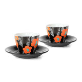 A pair of floral printed espresso cups and saucers. Each cup features a orange floral print on a black and white background. The saucers are black