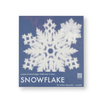 A lacy paper snowflake shows through clear packaging against a blue cardboard backing.