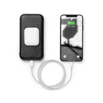  An AirPod case rests on top of the Carry, and a charging iPhone is plugged into the Carry with a looped white charging cable.