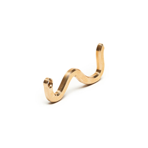 Squiggly small brass object standing on its side against a white background with opening on one end for key ring attachment.