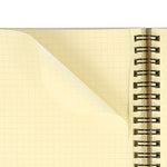 Close up of perforated cream graph pages with square holes threaded by a sturdy black metal spiral, showing a curled back, partially torn page.  