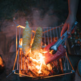 The  Splitter shown as a tong being used to flip salmon and corn on the cob over an outdoor grill.