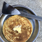 The spatula shown laying atop a pan with freshly made pancakes.