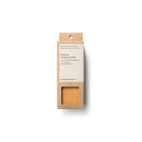 Rectangular, natural cardboard package with gray label for the Kitchen Cleaning Pad Anodized Aluminum, window-cut out reveals yellow, sandy-colored and textured cleaning pad.