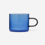 Low glass mug with a straight-sided blue bowl and a delicate, elongated, smoke-gray handle.