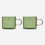 Two identical low glass mugs with straight-sided green bowls and a delicate, elongated, pale-pink handles.