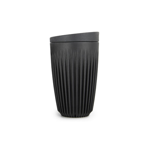 A tall, charcoal-colored reusable cup with a flat bottom, tapering shape and overall  pattern of tight vertical ribs, indented towards the base. With a flat, wedge-shaped lid.