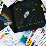 A child's drawing of a bird on black paper, surrounded by art supplies.
