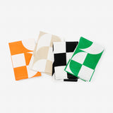 Four napkins, each folded to reveal a different portion of the same checker-wave pattern, each in a different color-and-white colorway—from left, orange, beige, black, green.